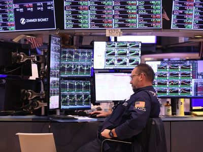 A trader sits at a desk in front of several computer screens on the floor of the New York Stock Exchange.