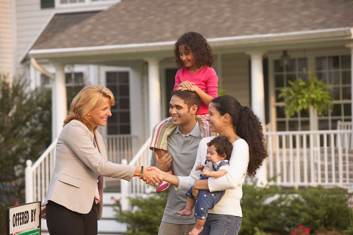 Hispanic family shaking hands with real estate agent in front of house
