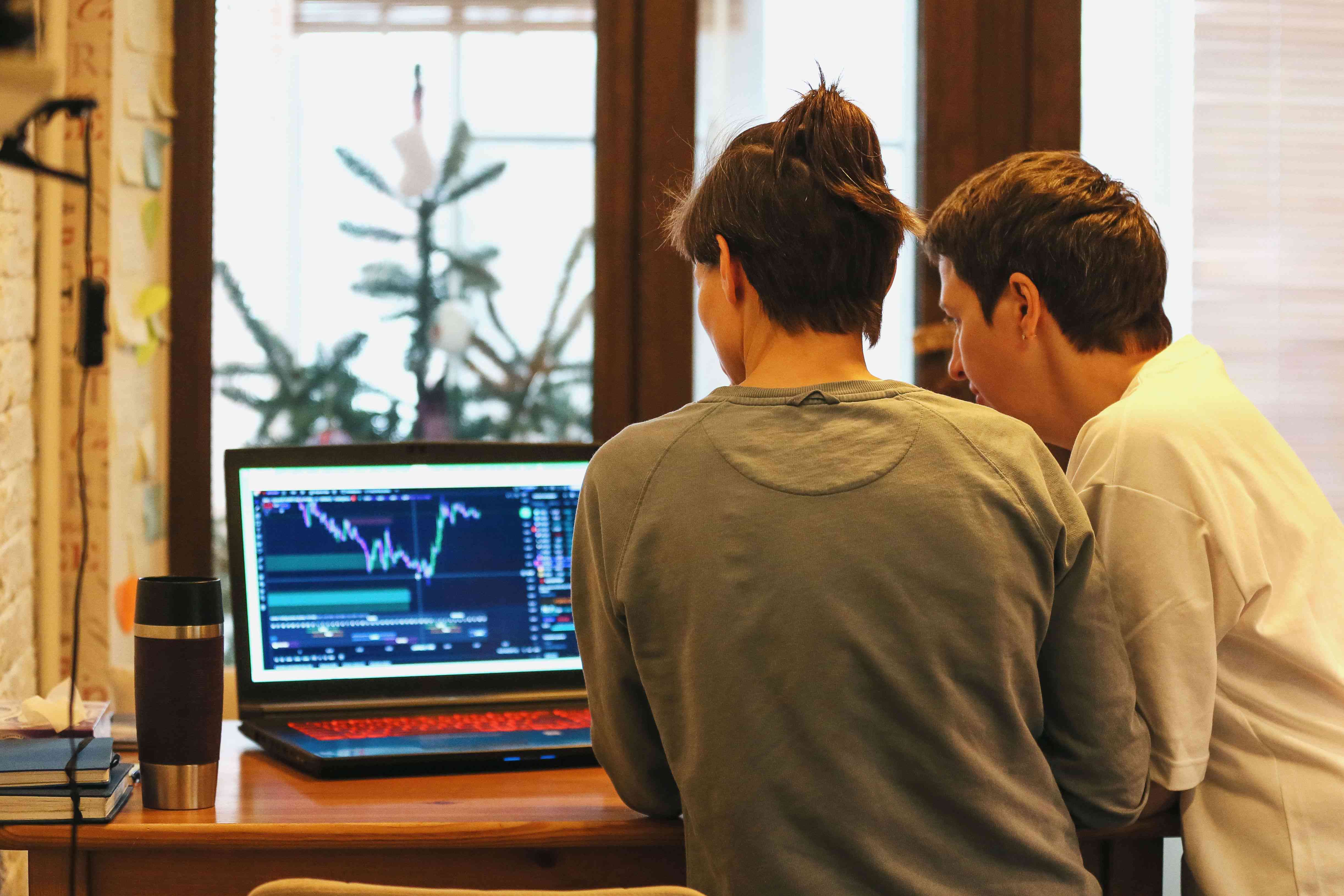Two people looking at market charts on a laptop at home