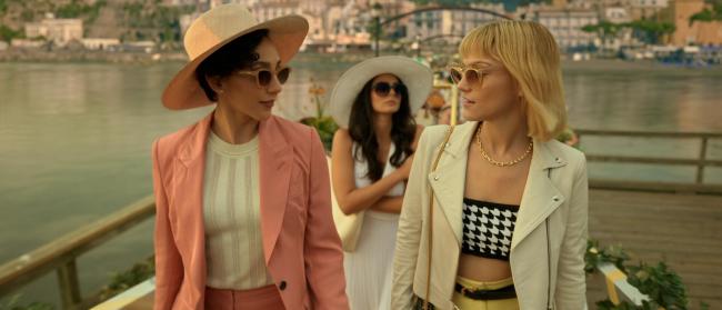 Three women dressed up while they walk along the doc in a seaside town; still from "Death and Other Details"