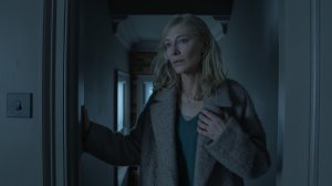 Cate Blanchett in 'Disclaimer' Episode 6, shown standing in an interior doorway wearing her brown coat