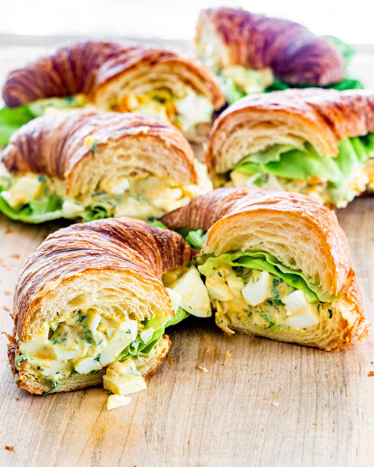 egg salad croissant sandwiches on a cutting board cut in half