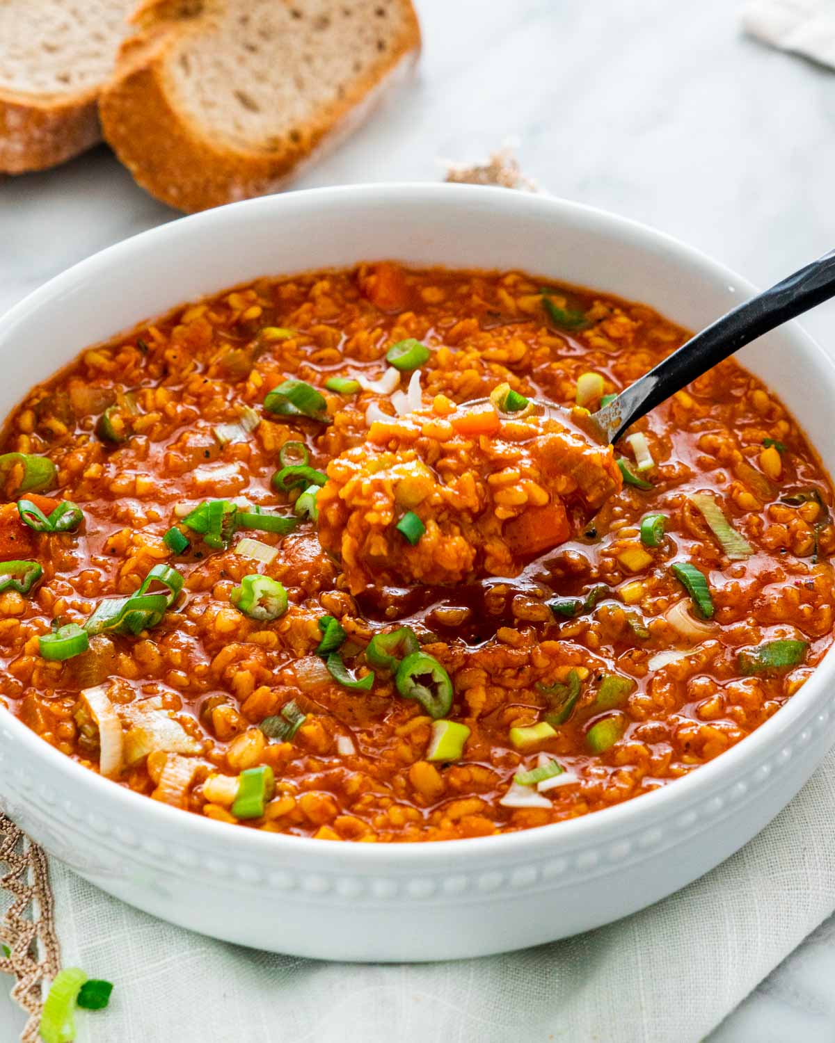 lentil soup in a  large white bowl garnished with green onions and a spoon spooning some out