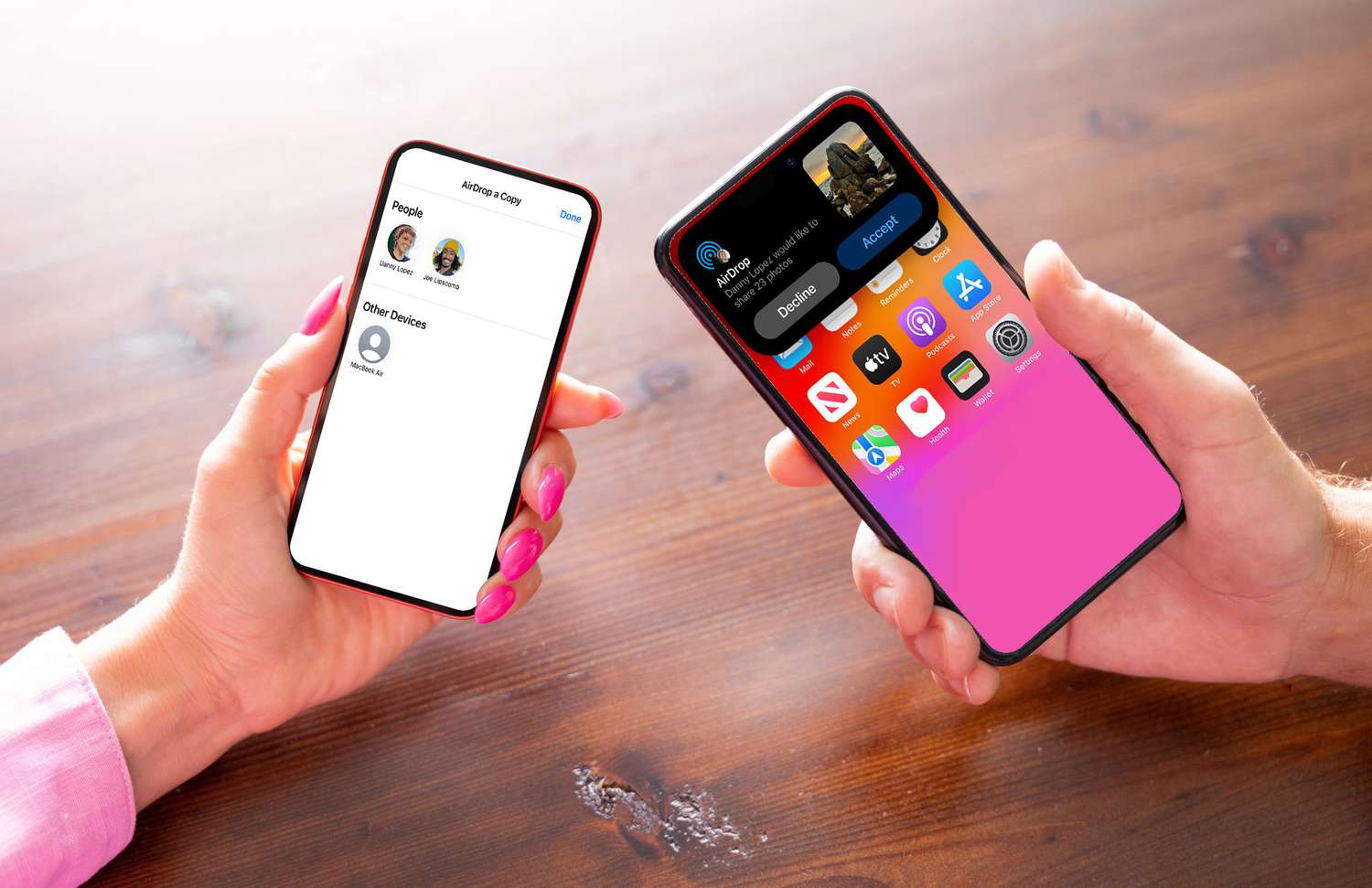 Two people holding phones over a wooden table. The AirDrop interface is open on both