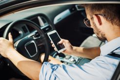 Man in driver's seat of car using smartphone.