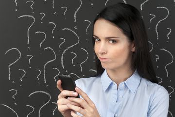 A person holding a phone in front of a blackboard of question marks