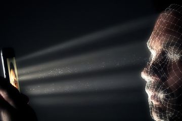 Man using face recognition on a mobile phone in a dark room.