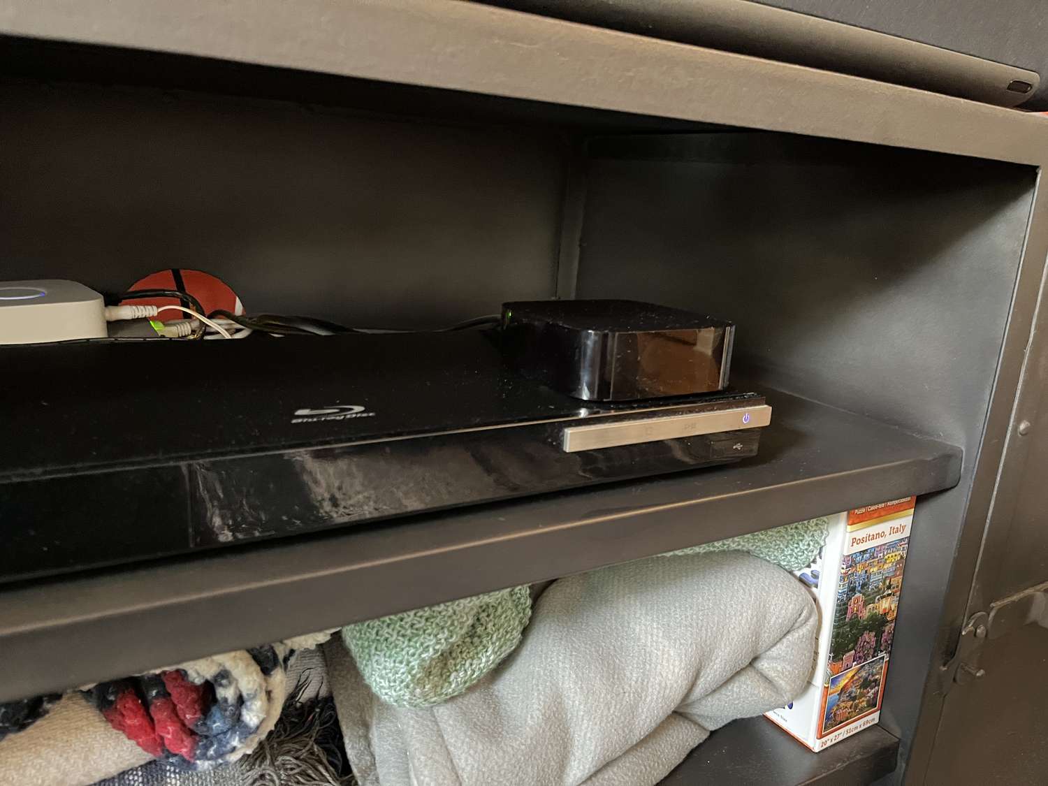 An Apple TV device on a shelf with other accessories and belongings.