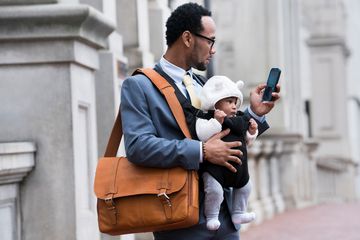 Businessman with glasses holding a bag, a baby, and an iPhone.