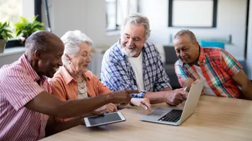 group of 4 seniors smiling looking at PC and tablet