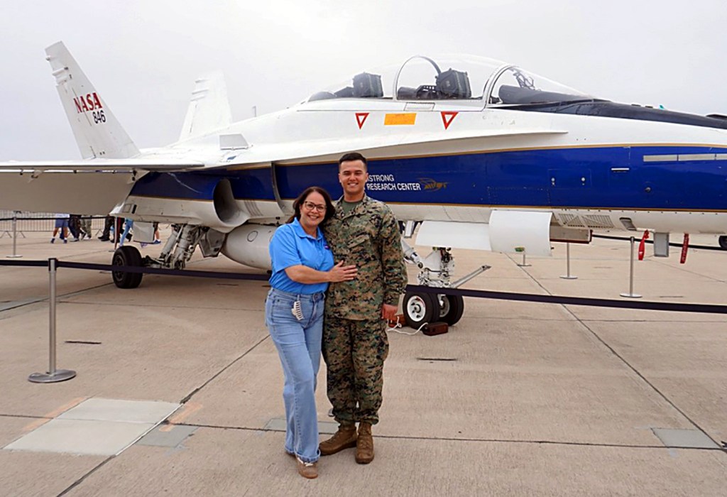 A man in military uniform and woman in NASA polo shirt stand in front of a NASA F/A-18 hornet aircraft.