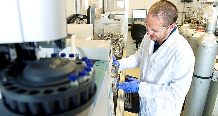 Photo of a man in a white lab coat and safety glasses working in a laboratory.