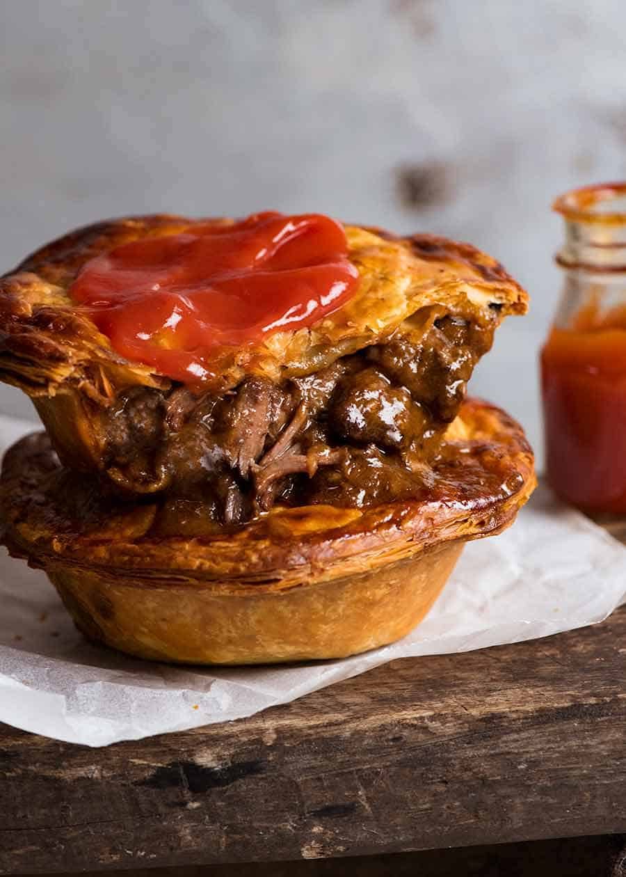 Two homemade Australian Meat Pies with tomato sauce, ready to be eaten