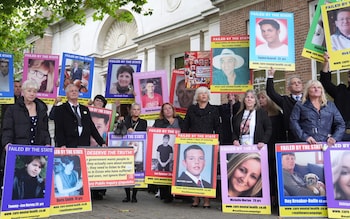 A group, wearing black clothes, holds up many placards showing the faces of their loved ones