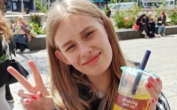 The teenager makes a victory V-sign with one hand and holds a cup of juice in the other, smiling