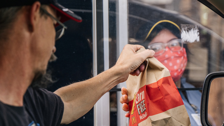 Man receives McDonald's order from a masked drive thru employee.