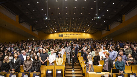 Viele Personen stehen in einem Hörsaal. 