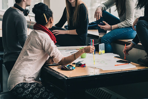 Students gathered around a table, discussing the best course of action for their project. Image by StockSnap from Pixabay