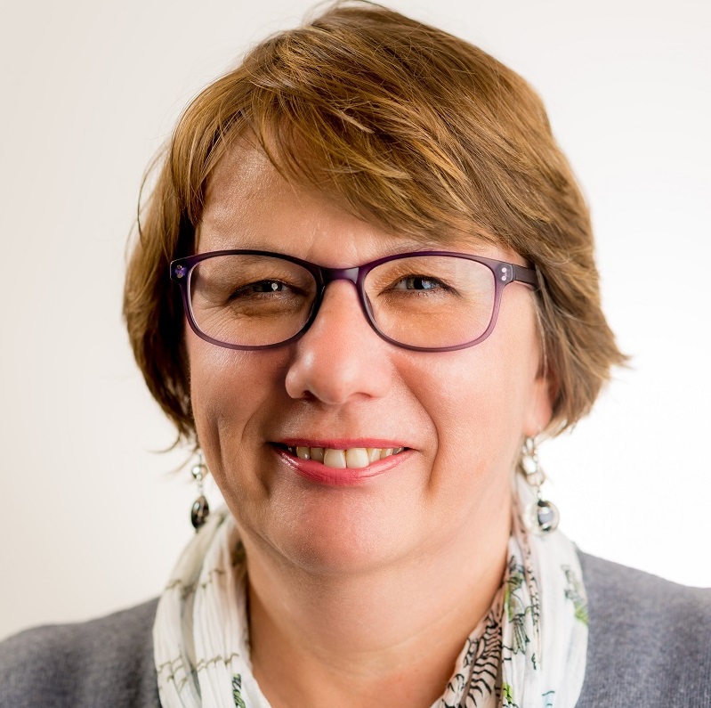 Headshot image of Jane Waite, a smiling middle-aged woman with light brown hair and purple-rimmed glasses.