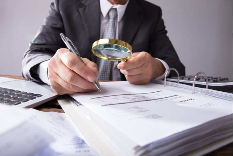 man examining documents with magnifying glass