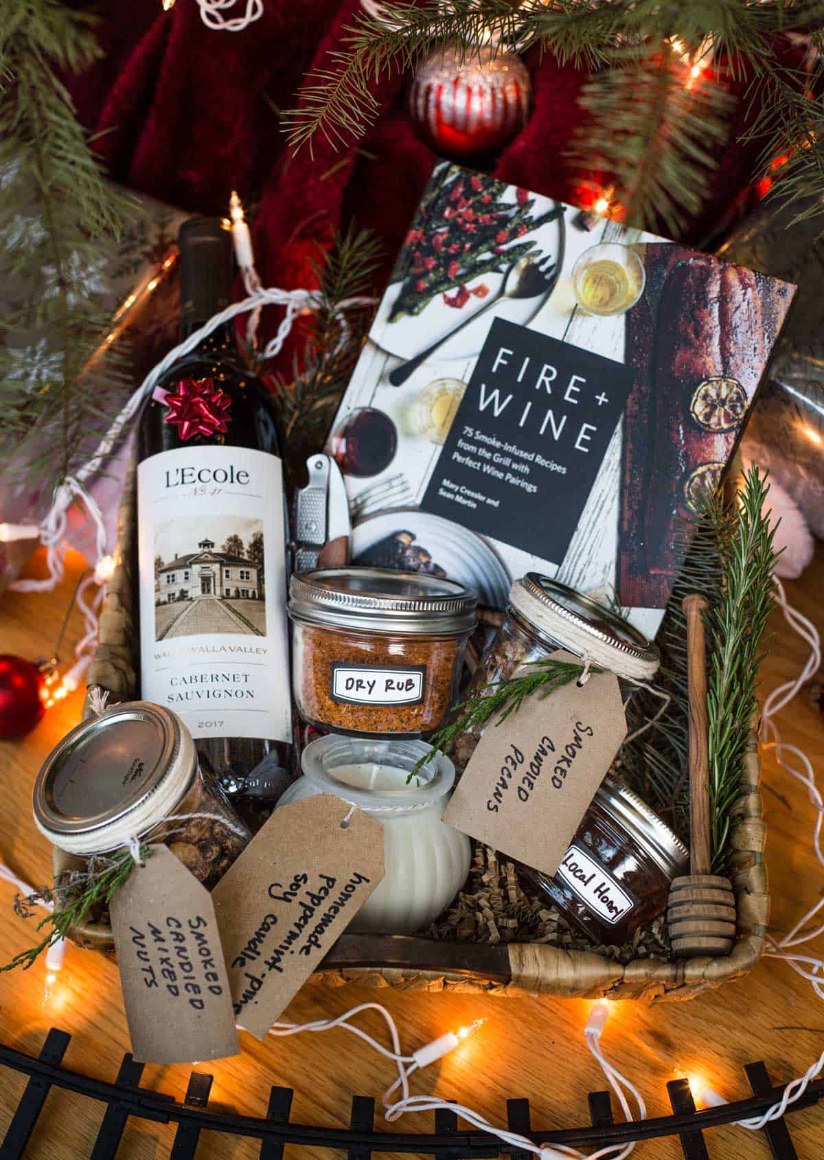 A holiday gift basket filled with edible gifts including L'Ecole wine, Fire + Wine cookbook, smoked mixed nuts, and other edible holiday gifts