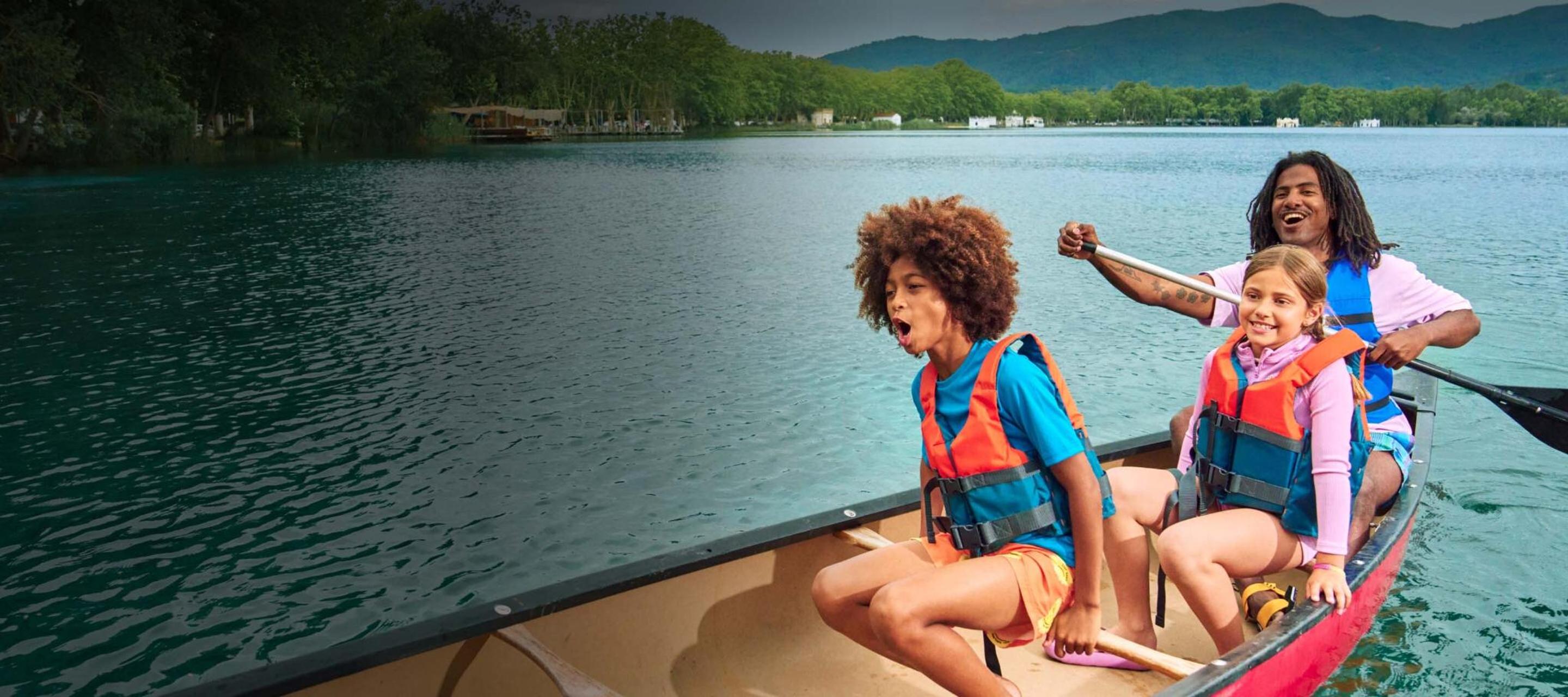 Two children and one adult laugh while canoeing across a lake. 