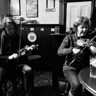 Two women playing fiddle in a pub.