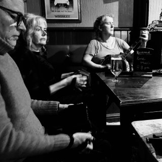 Two concertina players and a banjo player sitting at a table in a pub corner.