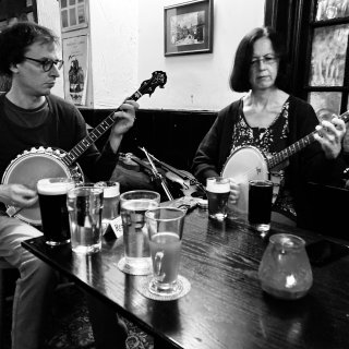 Two banjo players, a man and a women, playing at a pub table.