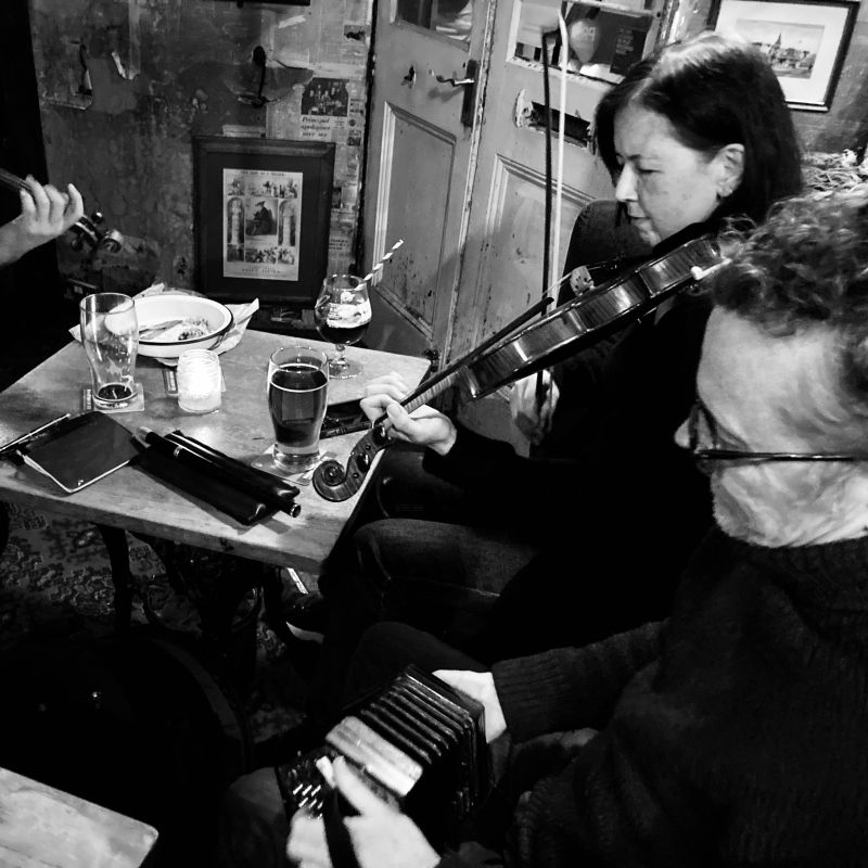 A man playing concertina and a woman playing fiddle at a table near the door of a pub.