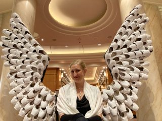 Jessica in black and white in front of angel wings made of pointe shoes.