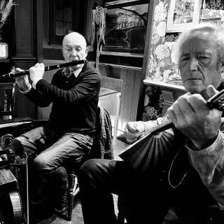 A man playing flute accompanied by a man playing Greek bouzouki in a pub.