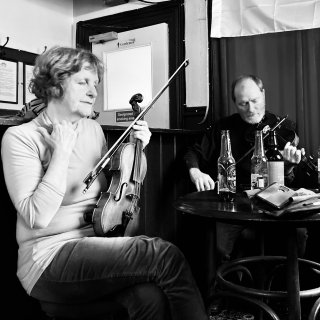 A man playing fiddle while a woman fiddler listens with her eyes closed.