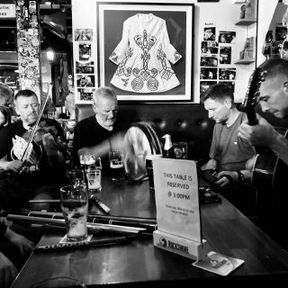 A fiddler, bodhrán player, concertina player and guitarist all playing at the end of a table.