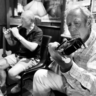 A man playing tin whistle accompanied by a man playing Greek bouzouki.