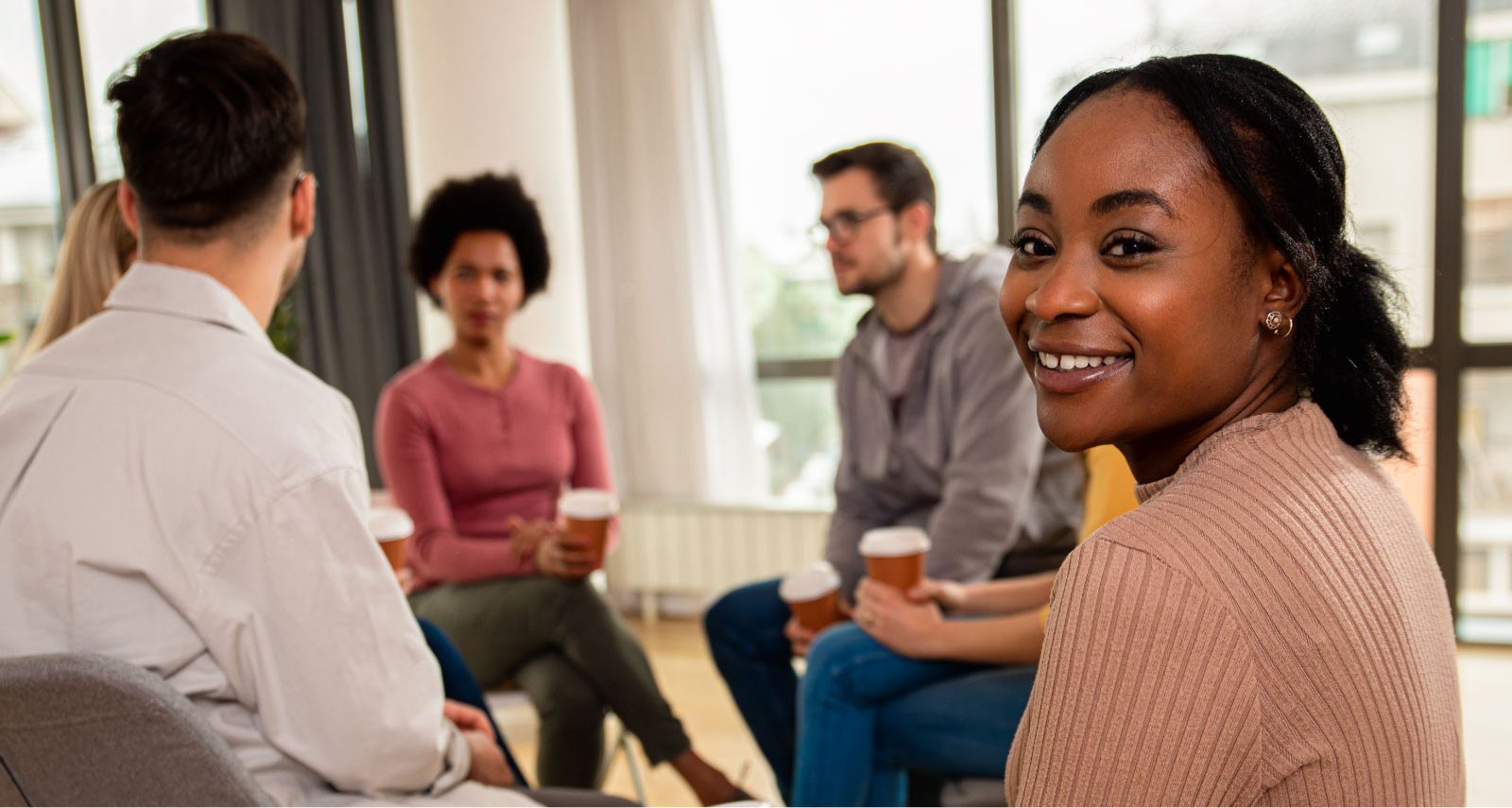 Group of people sat in a cirlce, with a woman looking at the camera