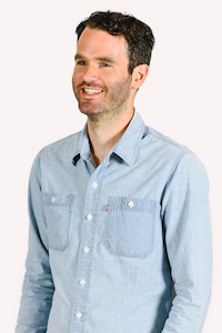 A white male with dark cropped hair wearing a blue shirt smiling and looking off to the left.