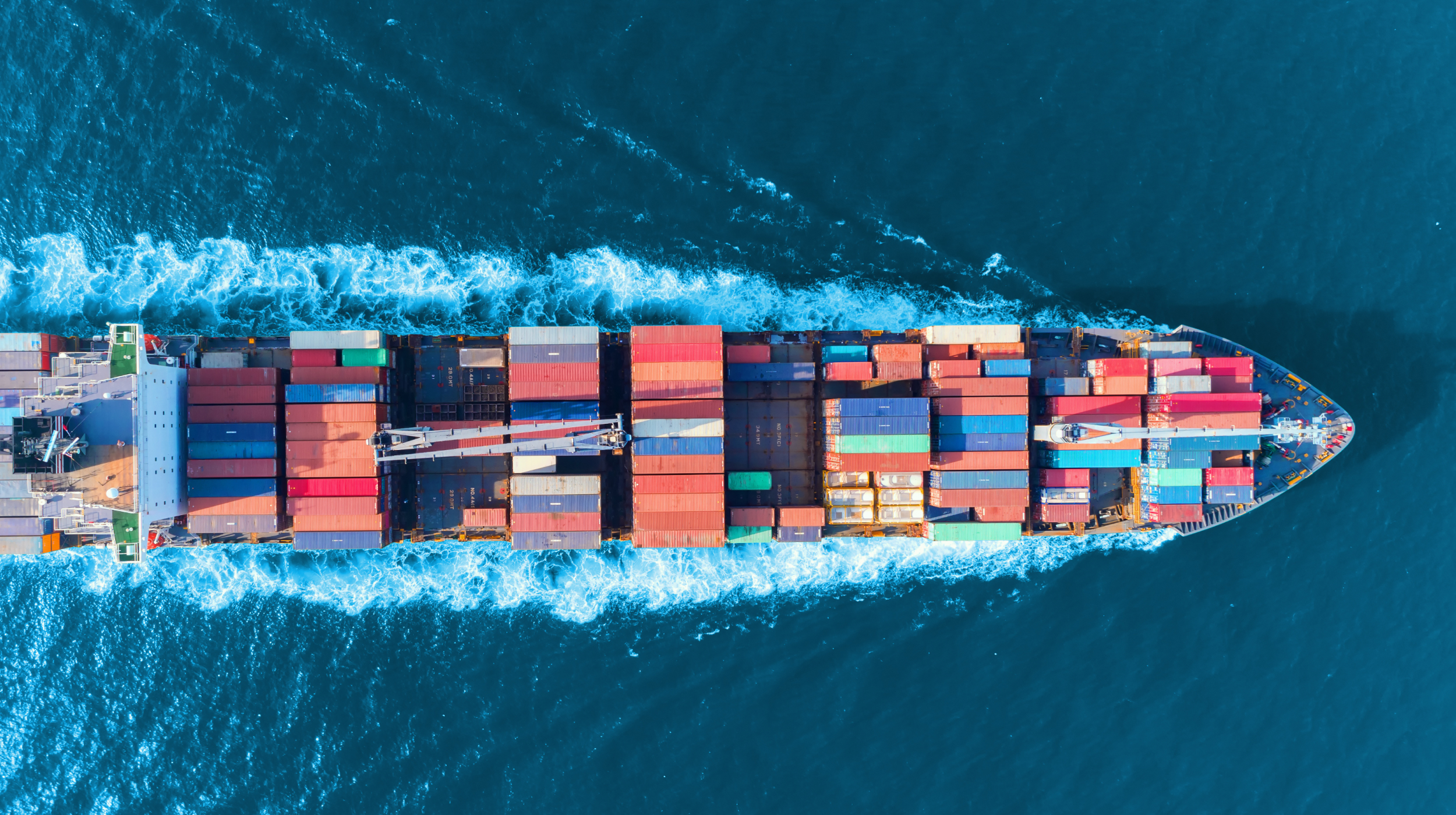 Aerial view of a large cargo ship with multicolored containers navigating through deep blue ocean waters.