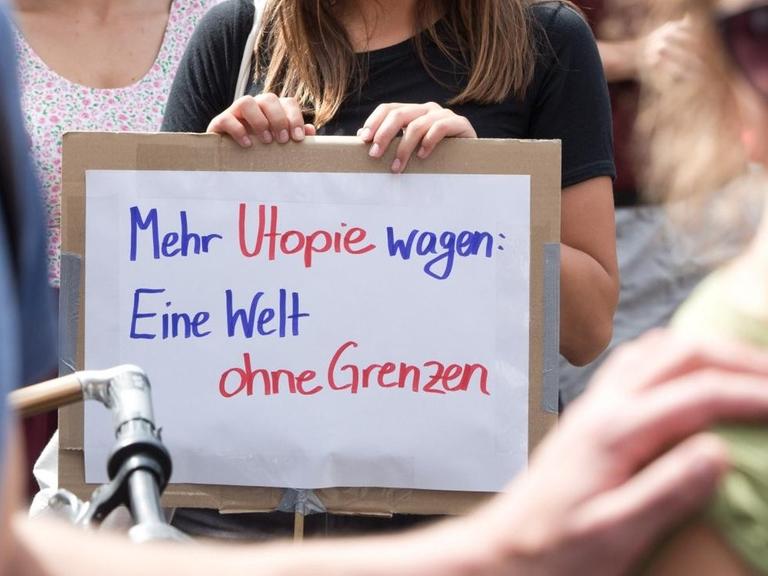 Eine Demonstrantin in Berlin-Kreuzberg hält bei Protesten für ein Bleiberecht für Flüchtlinge ein Schild mit der Aufschrift "Mehr Utopie wagen: Eine Welt ohne Grenzen". (5.7.2014)