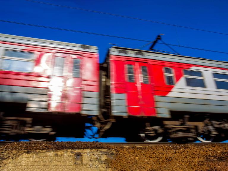 Zwei fahrende rote Waggons der Transsibirischen Eisenbahn auf einem Gleis. Sie fahren, dadurch hat das Bild eine Bewegungsunschärfe.