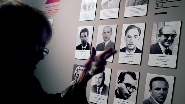 Eine Frau steht vor einer Ausstellungstafel. Darauf sind die Schwarz-Weiß-Bilder von Männern, die an der Entführung von Adolf Eichmann beteiligt waren.