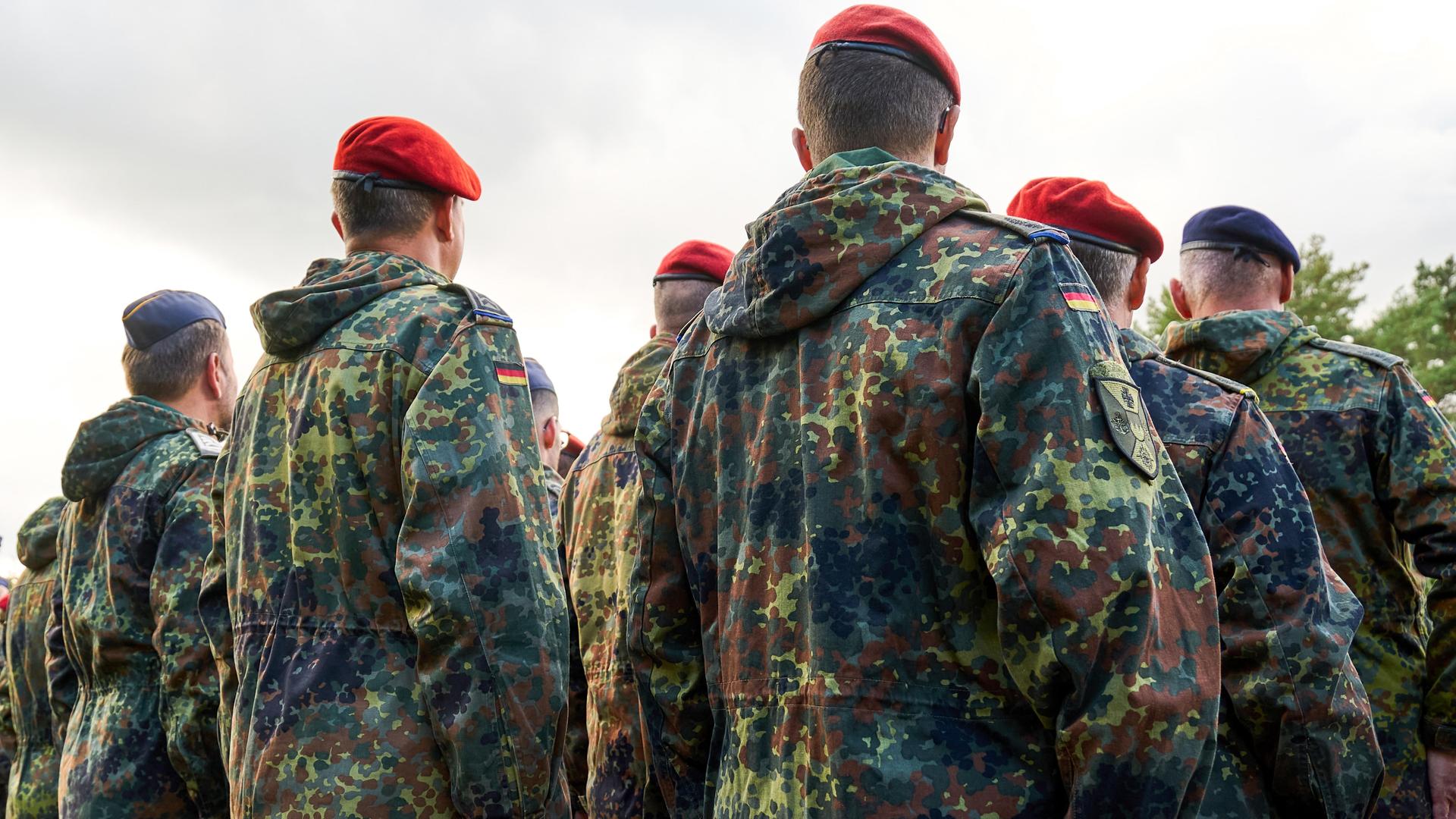 Soldaten der Bundeswehr stehen in Reih und Glied, gekleidet in Flecktarnuniformen und tragen rote sowie blaue Baretts