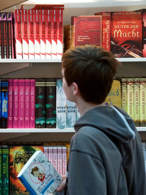 Kinder schauen sich Bücher in einem Regal an. 