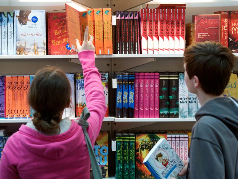 Kinder schauen sich Bücher in einem Regal an. 