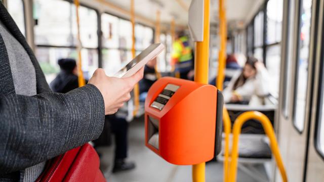 Eine Person bezahlt mit dem Smartphone in einer Straßenbahn.