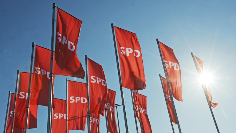 Rote Fahnen mit dem SPD Logo wehen vor einem Landesparteitag.