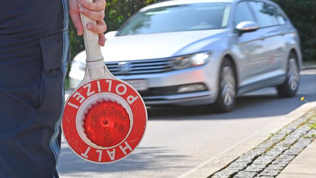 Ein Grenzpolizist hält eine Kelle, im Hintergrund ist ein Auto zu sehen.