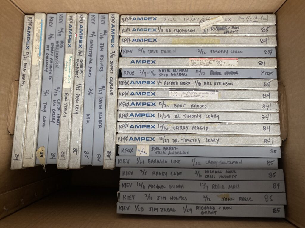 A view into a cardboard box filled with 27 smaller boxes, each carefully labeled with a radio station call letters, date, and interviewee name. For instance, KFOX - 12/28 - DR. TIMOTHY LEARY