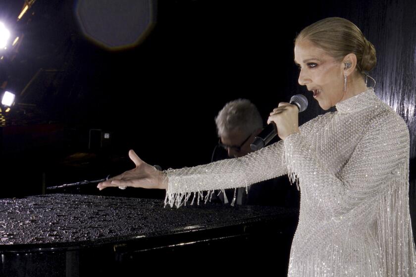 Celine Dion holds out her right hand while singing into a microphone in her left hand