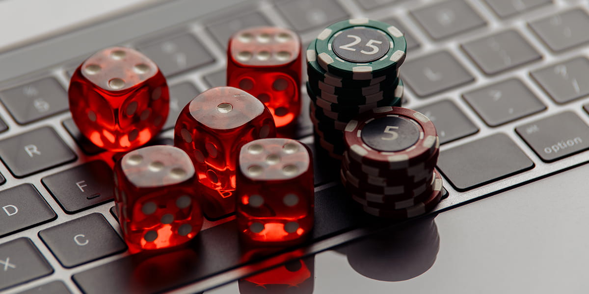 Online casino concept. Gambling chips and five red dices on laptop keyboard close-up